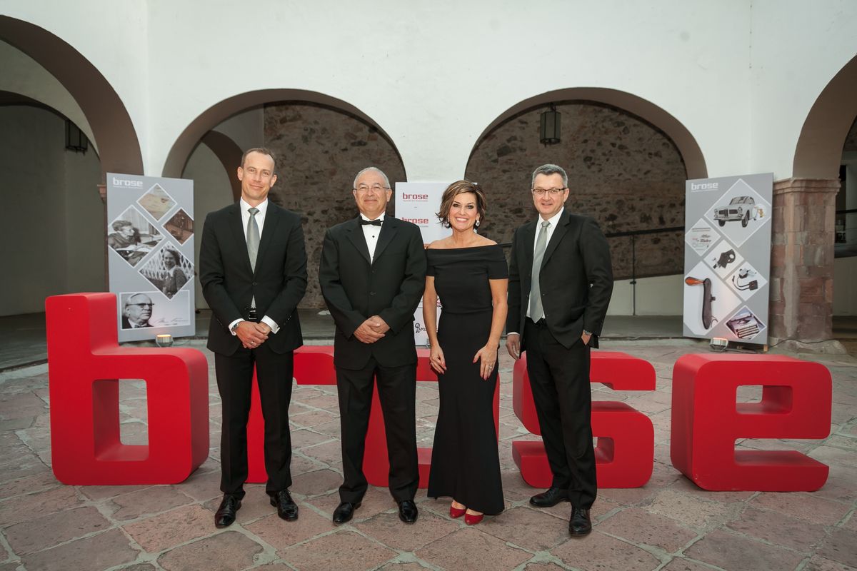 Brose executives in evening dress in front of large red 3D letters spelling brose in an arched courtyard