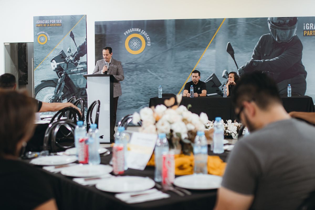 Head table and speaker at a lectern in front of BRP Educational Program panels with Can-Am motorcycle imagery, during the scholarship ceremony