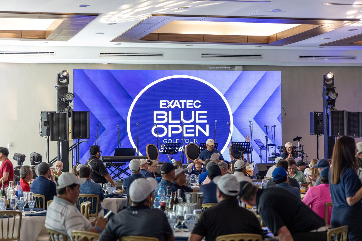 Banquet room with round tables, a stage with instruments and an LED screen showing the EXATEC Blue Open Golf Tour identity